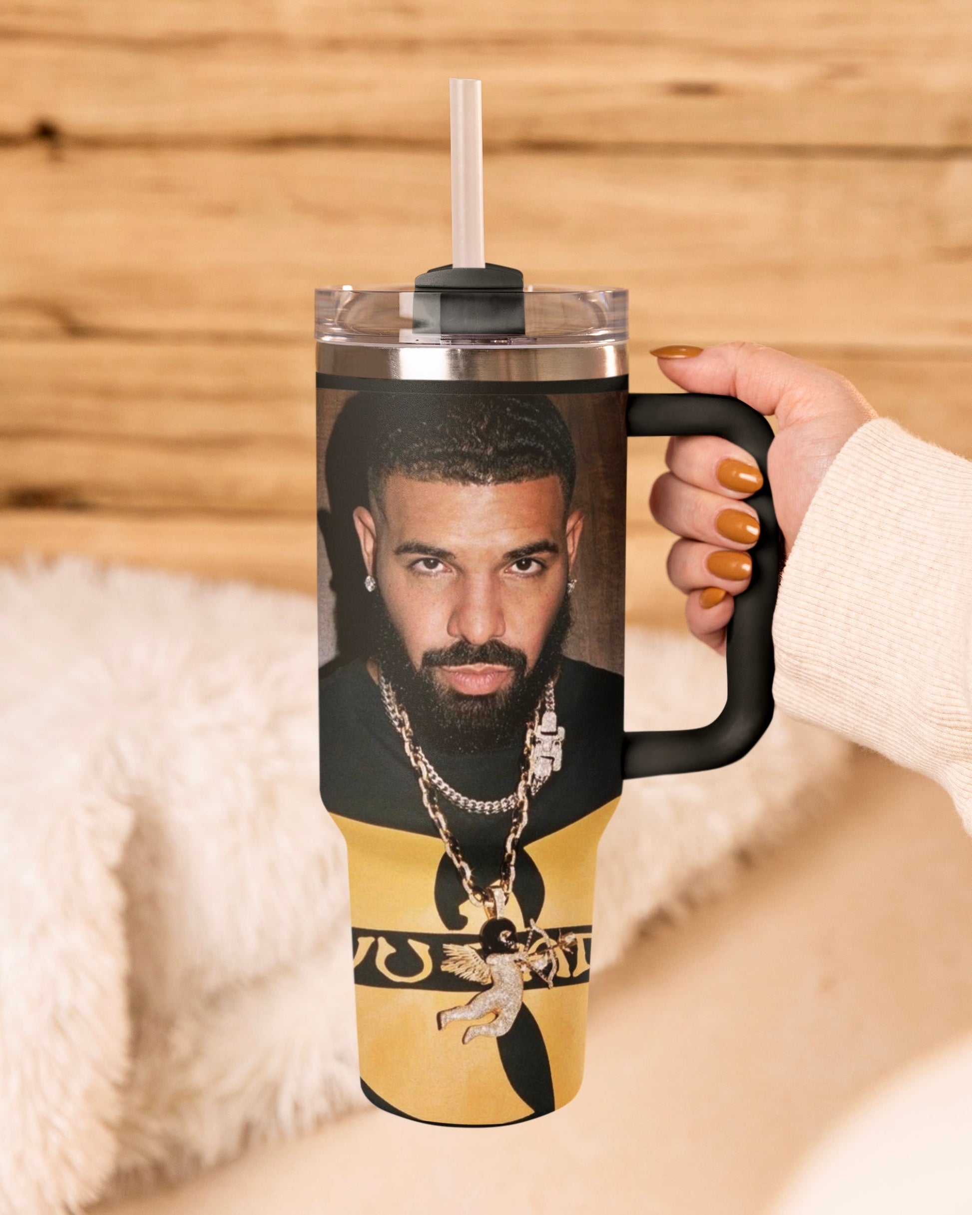 Tumbler with a Drake face printed on it, held by a hand against a wooden background.